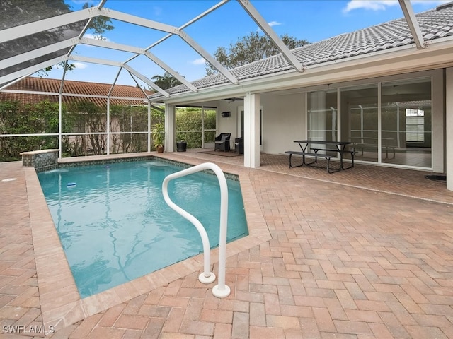 view of pool with glass enclosure, pool water feature, ceiling fan, and a patio