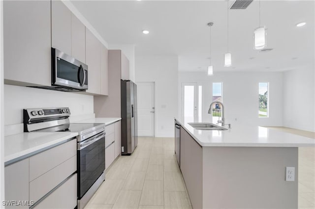 kitchen with gray cabinetry, sink, pendant lighting, a kitchen island with sink, and appliances with stainless steel finishes