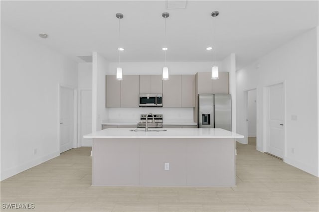 kitchen with sink, stainless steel appliances, pendant lighting, gray cabinets, and a center island with sink