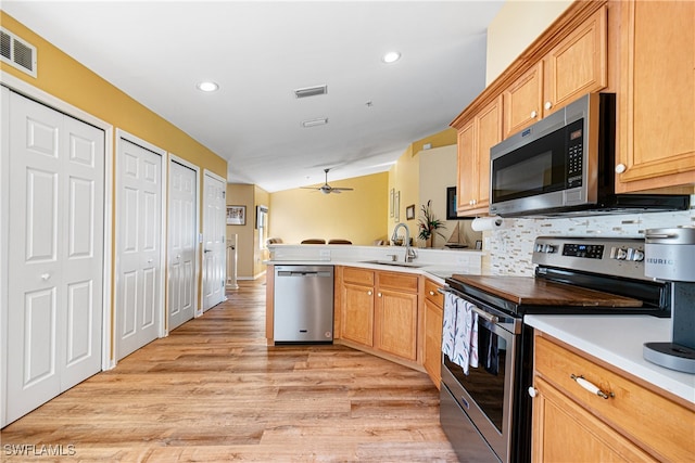 kitchen with decorative backsplash, appliances with stainless steel finishes, kitchen peninsula, sink, and light hardwood / wood-style floors