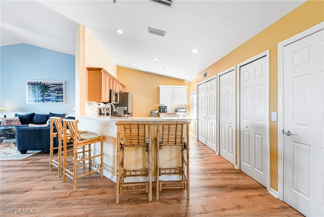 kitchen featuring lofted ceiling, light hardwood / wood-style floors, kitchen peninsula, and a breakfast bar