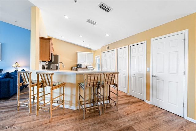 kitchen with kitchen peninsula, light wood-type flooring, sink, a breakfast bar area, and lofted ceiling