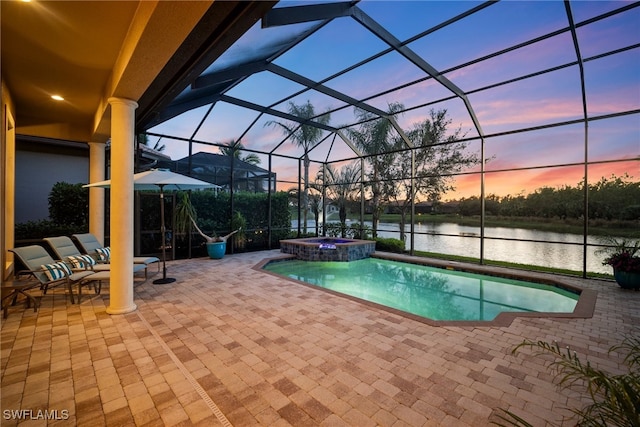 pool at dusk featuring glass enclosure, an in ground hot tub, a water view, and a patio