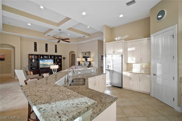 kitchen featuring white cabinets, light stone counters, stainless steel refrigerator with ice dispenser, and a large island with sink