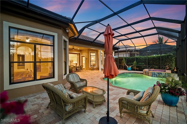 patio terrace at dusk with a lanai, outdoor lounge area, and an in ground hot tub