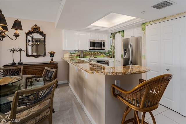 kitchen featuring a kitchen breakfast bar, stainless steel appliances, kitchen peninsula, light stone counters, and white cabinetry