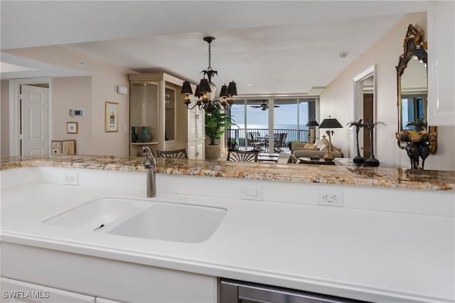 kitchen featuring light stone countertops, decorative light fixtures, an inviting chandelier, white cabinets, and sink