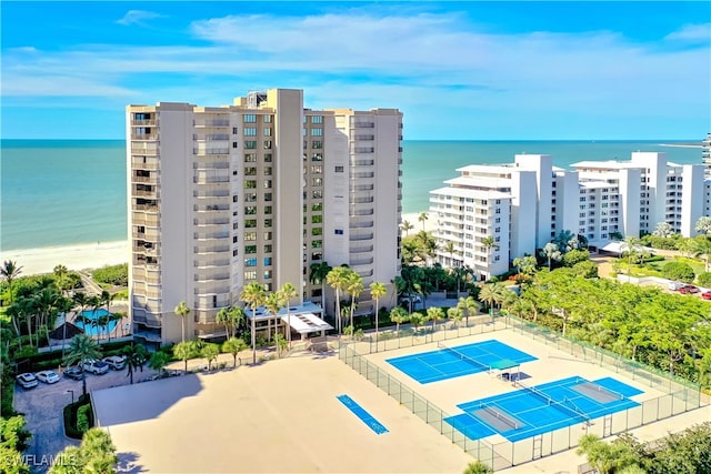 view of swimming pool with tennis court, a water view, and a view of the beach