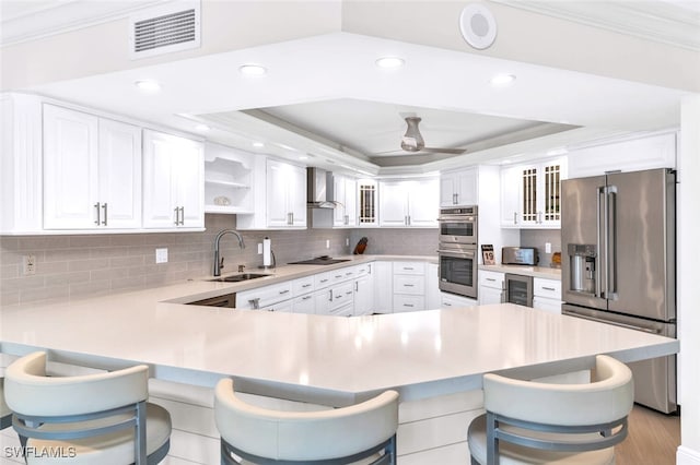 kitchen with sink, wall chimney range hood, kitchen peninsula, a kitchen bar, and appliances with stainless steel finishes