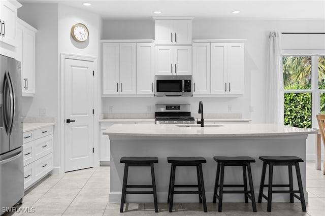 kitchen with appliances with stainless steel finishes, light tile patterned floors, white cabinetry, and a kitchen island with sink