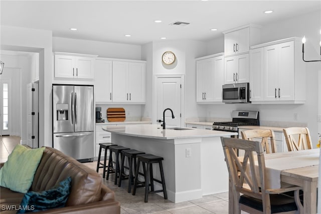 kitchen featuring a breakfast bar, a center island with sink, sink, white cabinetry, and stainless steel appliances