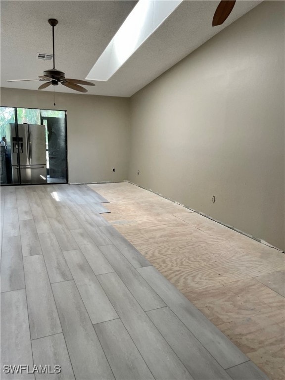 interior space with a skylight, ceiling fan, and light wood-type flooring