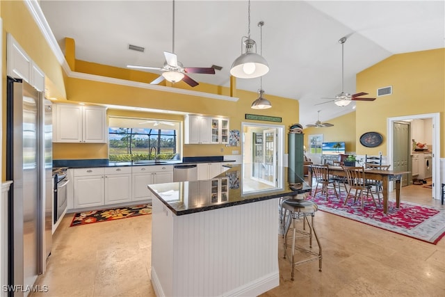 kitchen with a kitchen bar, stainless steel appliances, a kitchen island, decorative light fixtures, and white cabinetry