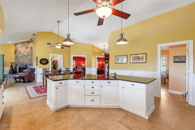 kitchen with dark stone counters, pendant lighting, high vaulted ceiling, white cabinetry, and a stone fireplace