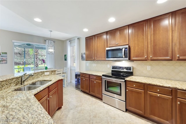 kitchen with decorative backsplash, appliances with stainless steel finishes, light stone counters, sink, and hanging light fixtures