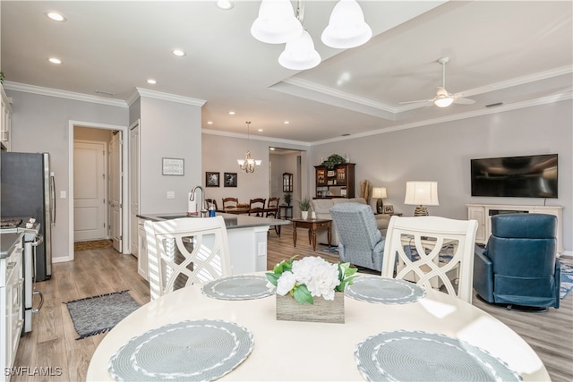 dining space with crown molding, sink, ceiling fan with notable chandelier, and light wood-type flooring