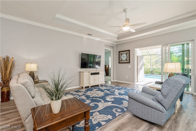 living room featuring hardwood / wood-style floors, ceiling fan, a raised ceiling, and crown molding