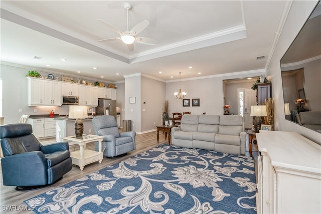 living room with a raised ceiling, ceiling fan with notable chandelier, light hardwood / wood-style flooring, and crown molding