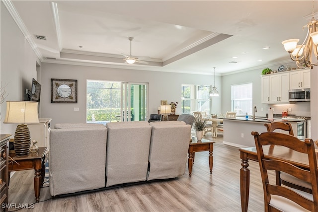 living room with ceiling fan with notable chandelier, a tray ceiling, light hardwood / wood-style flooring, and ornamental molding