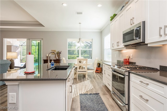 kitchen featuring a kitchen island with sink, sink, appliances with stainless steel finishes, decorative light fixtures, and light hardwood / wood-style floors