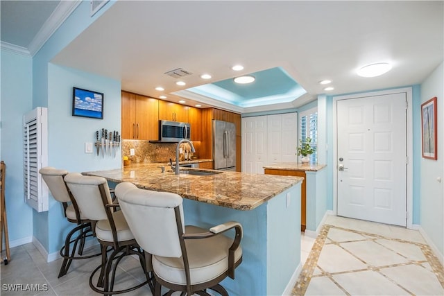 kitchen with light stone countertops, appliances with stainless steel finishes, sink, kitchen peninsula, and a breakfast bar