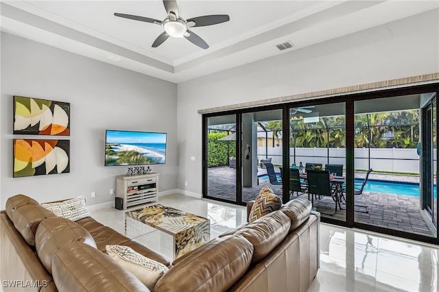 living room featuring a raised ceiling, plenty of natural light, ornamental molding, and ceiling fan