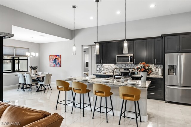 kitchen with decorative light fixtures, an island with sink, appliances with stainless steel finishes, and a breakfast bar area