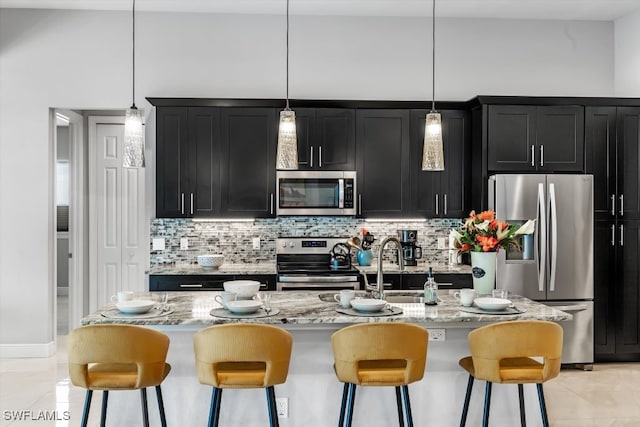 kitchen with a kitchen breakfast bar, a center island with sink, hanging light fixtures, and appliances with stainless steel finishes