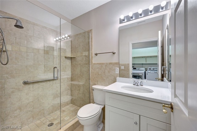 bathroom with walk in shower, vanity, separate washer and dryer, tile walls, and toilet