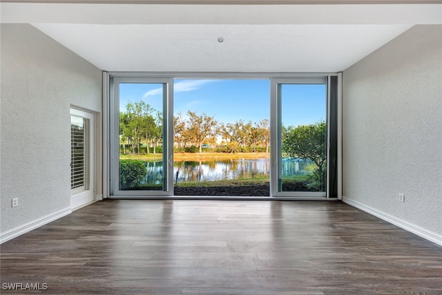 empty room featuring expansive windows, dark wood-type flooring, a water view, and a healthy amount of sunlight