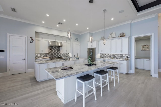 kitchen with ventilation hood, white cabinets, hanging light fixtures, stainless steel fridge, and a large island