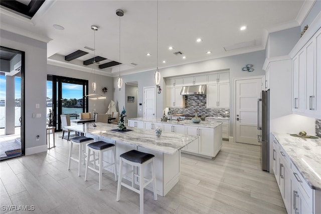 kitchen featuring decorative backsplash, light wood-type flooring, a large island with sink, decorative light fixtures, and white cabinets