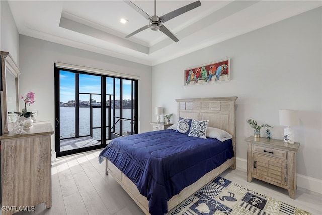 bedroom featuring access to exterior, ceiling fan, a tray ceiling, a water view, and light wood-type flooring