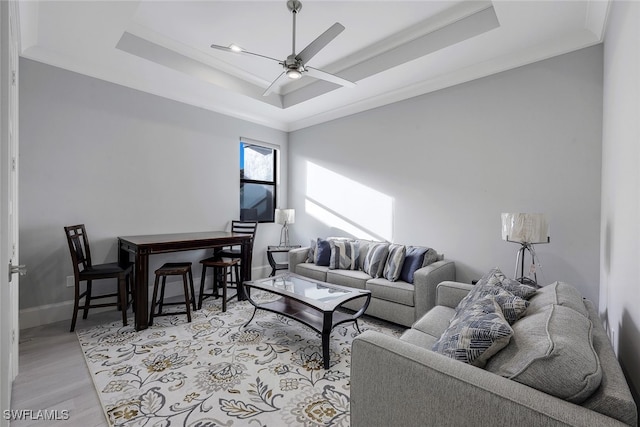 living room featuring a raised ceiling, ceiling fan, crown molding, and light wood-type flooring