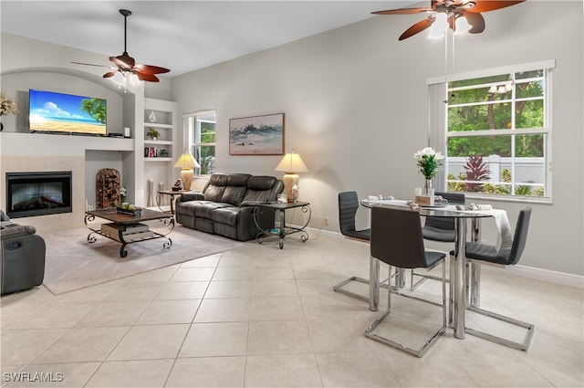 living room with a tile fireplace, light tile patterned floors, ceiling fan, and built in shelves