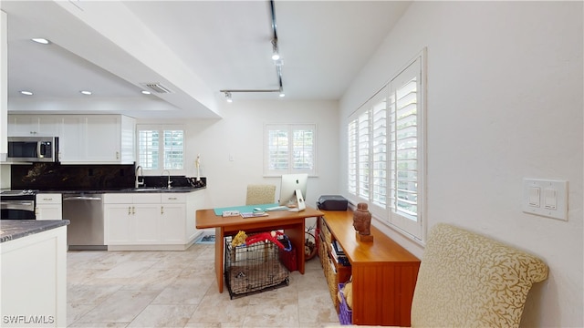 kitchen with appliances with stainless steel finishes, rail lighting, sink, light tile patterned floors, and white cabinets