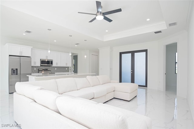 living room featuring ceiling fan, ornamental molding, sink, and a tray ceiling