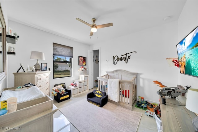 bedroom featuring a nursery area and ceiling fan