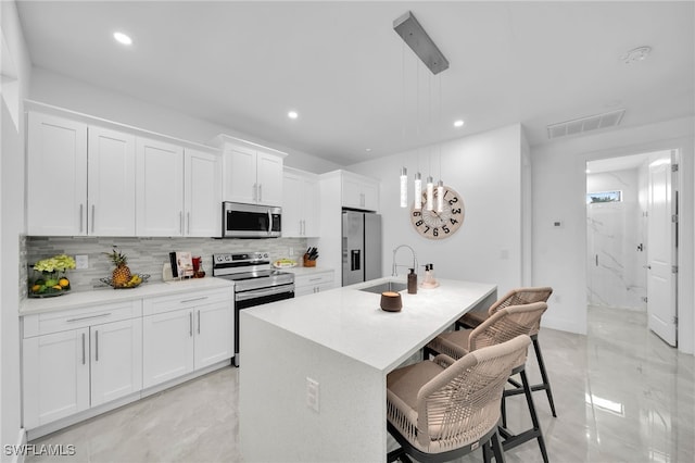 kitchen featuring stainless steel appliances, sink, a center island with sink, white cabinetry, and hanging light fixtures