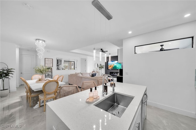 kitchen featuring ceiling fan with notable chandelier, sink, pendant lighting, a center island with sink, and white cabinetry