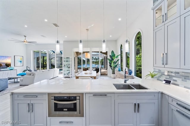 kitchen featuring tasteful backsplash, light stone counters, sink, decorative light fixtures, and oven