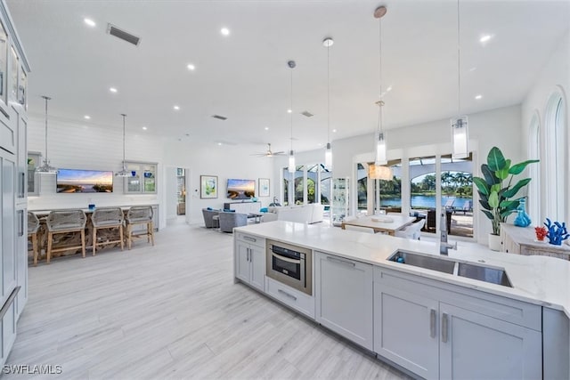 kitchen featuring gray cabinetry, ceiling fan, hanging light fixtures, oven, and light wood-type flooring