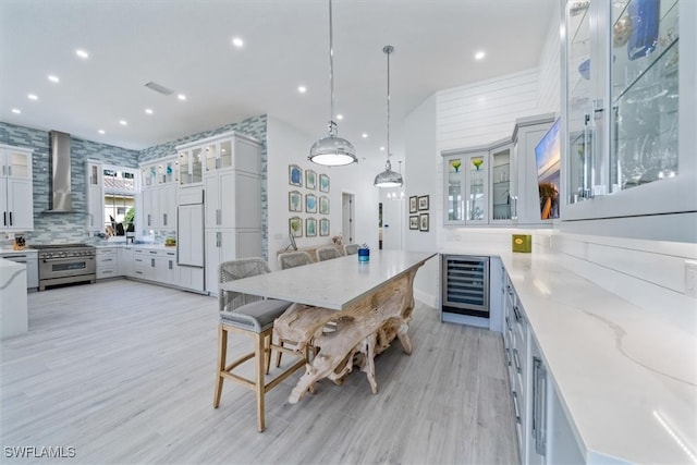 kitchen featuring high end appliances, wall chimney range hood, hanging light fixtures, wine cooler, and light stone counters