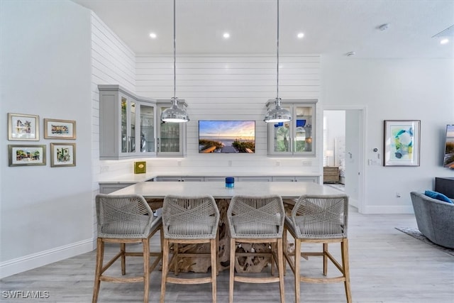 kitchen with a kitchen breakfast bar, gray cabinetry, light hardwood / wood-style flooring, and decorative light fixtures