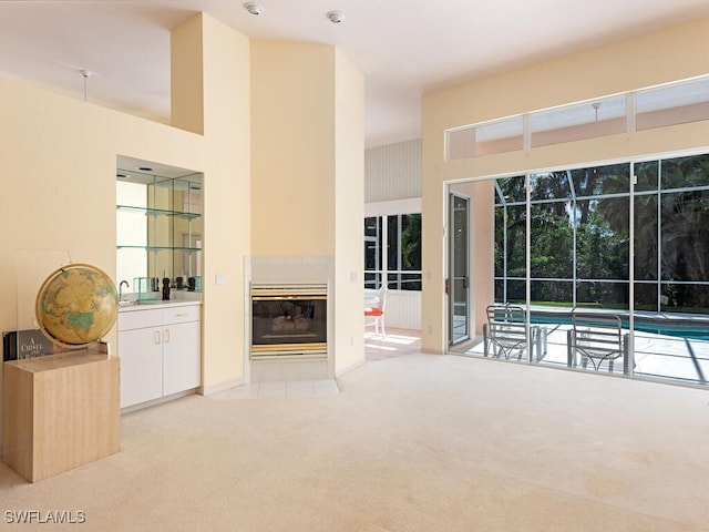 unfurnished living room featuring light colored carpet, a high ceiling, and a tiled fireplace