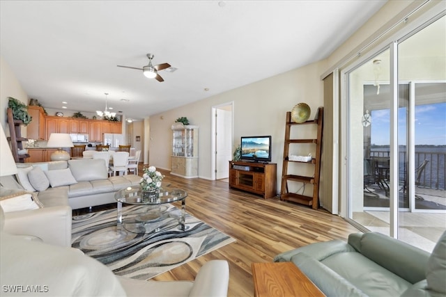 living room with ceiling fan with notable chandelier and light hardwood / wood-style flooring