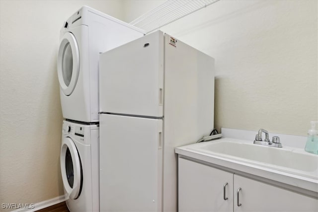 clothes washing area with cabinets, sink, and stacked washing maching and dryer