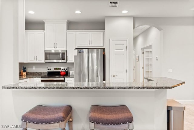 kitchen featuring white cabinetry, stainless steel appliances, kitchen peninsula, and a breakfast bar area