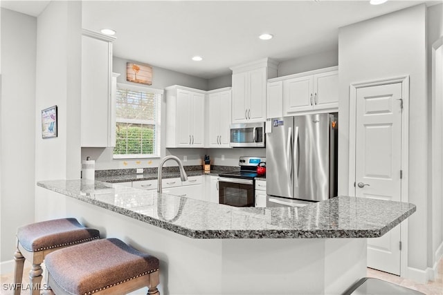 kitchen with sink, kitchen peninsula, stone counters, stainless steel appliances, and white cabinets