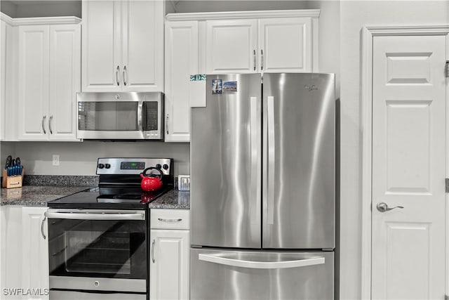 kitchen with appliances with stainless steel finishes, white cabinets, and dark stone counters